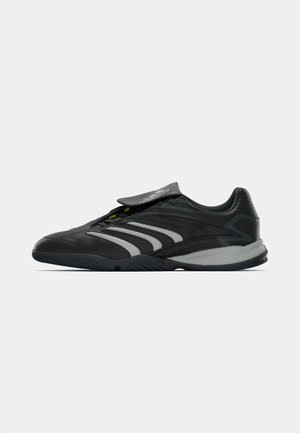 Czarne sportowe buty z szarymi i białymi paskami, niskoprofilową podeszwą oraz rzepem zasłaniającym sznurówki na jednolitym tle.