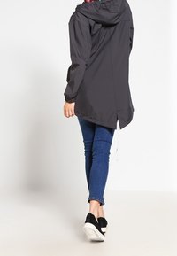 Czarna wodoodporna kurtka z kapturem, z kwiecistą podszewką, elastycznymi mankietami i ściągaczem na dole. Połączona z niebieskimi dżinsami i czarnymi trampkami.