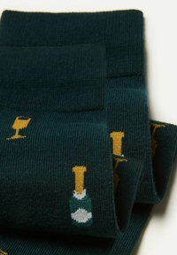Calcetines de color verde oscuro con un patrón repetido de copas de champán amarillas y botellas verdes con acentos blancos. Diseño de canalé texturizado.