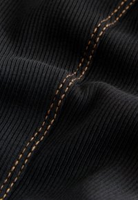 Gros plan sur un tissu noir côtelé avec une double surpiqûre orange proéminente le long d'une couture courbée.