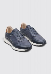 Zapatillas de color azul marino con una combinación de cuero liso y perforado, suelas blancas y detalles en cuero marrón en el talón. Presentan cordones elásticos.