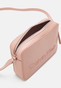 Prostokątna torba na ramię Calvin Klein z miękkiej, różowej skóry, wyposażona w zamek błyskawiczny, tłoczone logo oraz wąski, regulowany pasek.