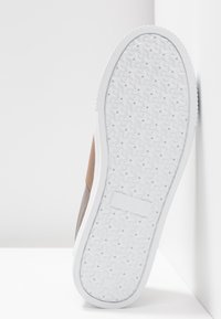 Chaussure à dessus en daim marron avec une semelle en caoutchouc blanche présentant un motif texturé. Les bords de la semelle sont légèrement arrondis.