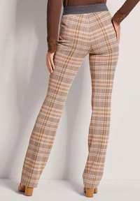 Plaid trousers in beige, pink, and brown tones; features a grey elastic waistband and a flared leg design with a smooth texture.