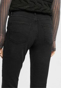 Jeans de mezclilla negra con un corte ajustado, que cuentan con dos bolsillos traseros y una textura suave, combinados con una camiseta de manga larga con textura.