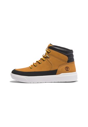 Bota alta en ante marrón con acentos negros, suela de goma blanca y cordones amarillos. Presenta un logo en el talón y una superficie texturizada.