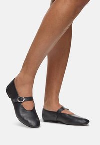 Ballerines en cuir noir de type Mary Jane, présentant un bout arrondi, un talon plat et une sangle avec une boucle circulaire en argent.
