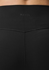 Svarta träningsleggings med en slät textur, prydda med en subtil "PIECES"-logotyp och stickade detaljer längs sömmarna.