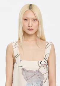 Hihaton mekko vaaleasta beige-kankaasta, jossa on abstrakteja kukka- ja viivakuviota, neljän kulman pääntie ja leveät olkaimet.
