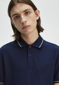 Polo de color navy con tejido texturizado, que cuenta con una tapeta de dos botones, rayas de contraste en el cuello y las mangas, y un pequeño logo en el pecho.