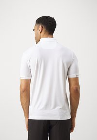 Λευκό πόλο μπλουζάκι με υφή, κοντά μανίκια και δύο μαύρες οριζόντιες ρίγες στις μανσέτες. Διαθέτει ευθεία γιακά και ραφή πίσω.