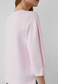 Hellrosa Sweatshirt mit dreiviertel Ärmeln, rundem Ausschnitt und Seitenschlitzen; gefertigt aus weichem, glattem Stoff mit dezenter Textur.