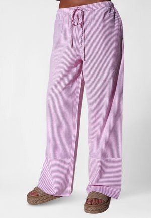 Vrouw draagt losse roze en witte verticale gestreepte broek met een taillekoord en gevlochten platformsandalen.