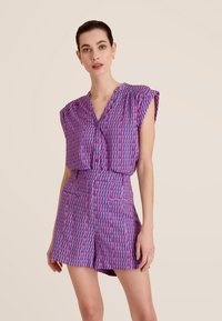 Robe à manches courtes et col en V, présentant un motif géométrique dans des teintes de violet et de rose. Coupe ajustée avec deux poches avant et une texture de tissu lisse.