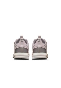 Des chaussures de sport légères rose pâle et grises en matériau en maille, de forme arrondie et avec des semelles blanches plates. Elles disposent de boucles à l'arrière pour faciliter l'enfilage.