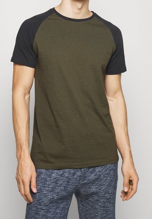 Camiseta de manga corta color verde oliva con mangas raglán negras, cuello redondo y textura suave, combinada con pantalones jogger azul jaspeado.