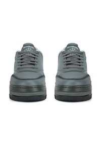 Sivé tenisky s hladkým koženým zvrškom, okrúhlou špičkou a hrubou čiernou podrážkou. Majú sivé šnúrky a logo na jazyku.