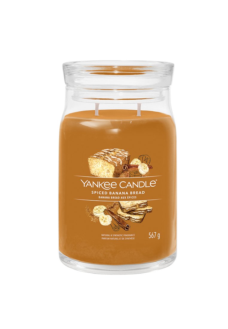 Durchsichtiger Glasbehälter mit zwei Baumwolldochten, gefüllt mit braunem Wachs. Das Etikett zeigt Illustrationen von Bananenbrot, Zimt und Bananen. 567 g.