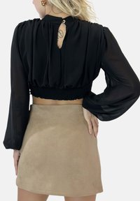 Top corto nero con maniche a palloncino, orlo arricciato e dettaglio in apertura a chiave sul retro; abbinato a una mini gonna in suede beige. Texture liscia e design attillato.