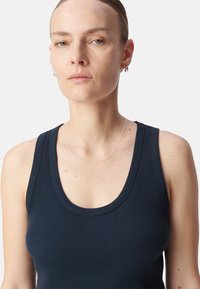 Camiseta sin mangas de canalé en color marino con escote redondeado. La tela es suave, ajustada y tiene un tejido texturizado. Acentuada con un fino collar plateado.