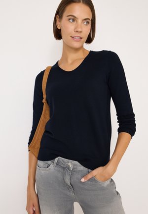 Pull en tricot bleu marine à col rond et manches trois quarts, associé à un jean en denim gris clair. La texture semble lisse.