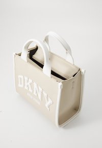 Krémszínű kézitáska fehér díszítéssel, dupla fogantyúkkal és cipzáras belső résszel. Az elülső oldalon feltűnő "DKNY NEW YORK" logó található.