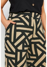 Pantalones de pierna ancha en negro y beige con un patrón geométrico abstracto. Hechos de un material texturizado, cuentan con bolsillos laterales y una cintura alta.