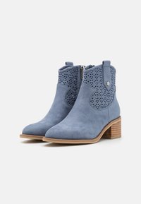 Botines de ante azul con detalles perforados, punta afilada y tacón apilado. Presentan una cremallera lateral y acentos texturizados.