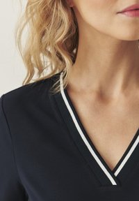 Haut bleu marine en V avec une bordure blanche. Confectionné en tissu doux, il présente une coupe décontractée et une texture lisse avec un design casual.
