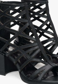 Zwarte hakken sandalen met een intricaat latticeontwerp en uitsparingen. Gladde lederen materiaal, rechthoekige hak en een glanzende binnenzool.