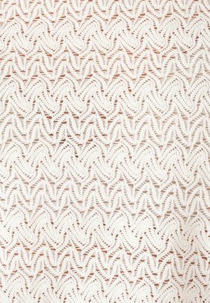 Nahaufnahme eines weißen gestrickten Stoffes mit sich wiederholendem Zickzack- und Spitzenmuster, das strukturierte Wellen erzeugt.