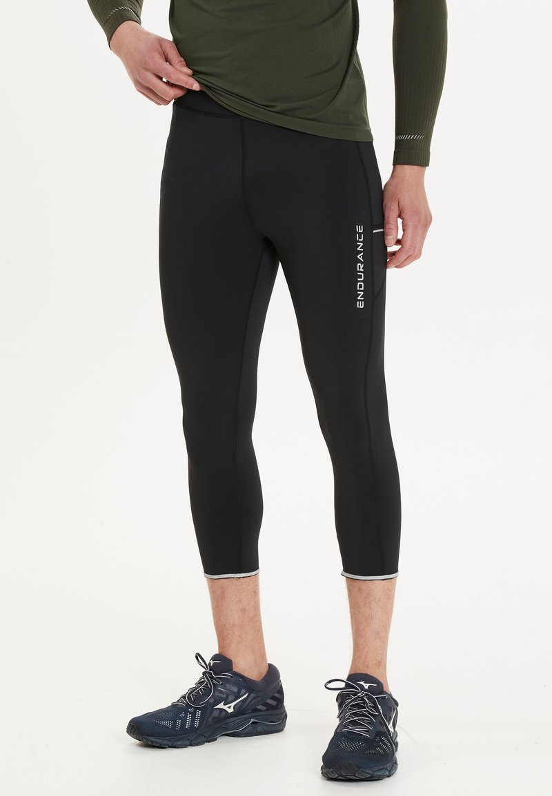 Svarta gymnastikleggings med en figurnära design, ankellängd, vit "ENDURANCE" branding på vänster sida och en slät, elastisk textur.