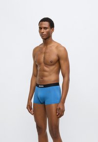 Blauwe boxershorts met een zwarte tailleband waarop het merk "BOSS" in witte letters staat. Soepele textuur, nauwsluitend ontwerp, mid-lengte model.