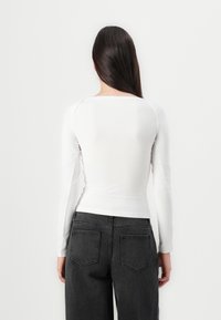 Fehér, hosszú ujjú póló, kerek nyakkivágással, slim fit szabással, párosítva magas derekú fekete farmernadrággal, amelyen két hátsó zseb és texturált felület található.