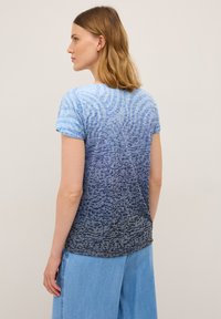 Modrá ombre tričko s jemnou texturou, s vlnitým vzorem. Krátké rukávy a zaoblený lem doplňují uvolněný střih.