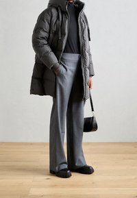 Doudoune gris foncé avec une capuche et des zips, assortie à un pantalon léger gris clair et des chaussures à plateforme noires épaisses. Petit sac.