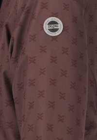 Bordeaux jakke med et subtilt zigzag-mønster, glat tekstur og et rundt sølv-logo med indskrifterne "ZIGZAG" og "ACTIVE LIFESTYLE".
