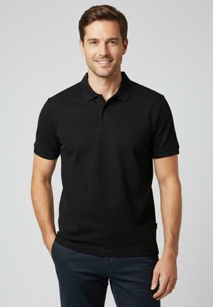 Zwart poloshirt met een gestructureerde stof, korte mouwen en een kraag met knopen. Draagt bijpassende marineblauwe broek. Eenvoudig ontwerp zonder patronen.