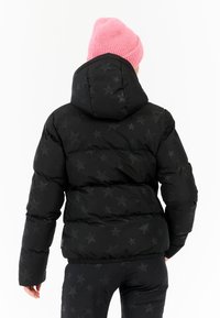 Zwarte pufferjack met een sterrenpatroon, voorzien van een capuchon en een elastische onderrand, gecombineerd met een roze gebreide muts.