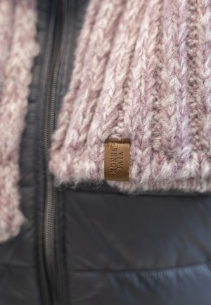 Knitted scarf in light pink and white hues, with chunky texture, attached leather tag, and worn over a dark, padded jacket.