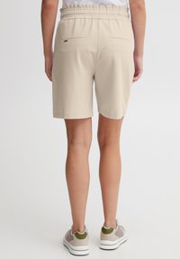 Shorts beige avec une taille élastique, deux poches arrière et une coupe décontractée. Texture lisse et design longueur genou.