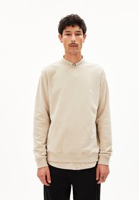 Helles beige Sweatshirt mit hohem Kragen, gerippten Bündchen und einem dezenten Logo auf der Brust. Hergestellt aus weichem, Baumwoll-Mischgewebe.