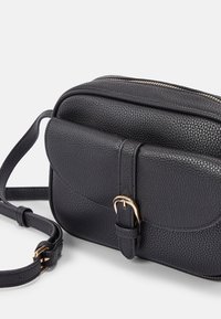 Bolso de hombro negro de cuero con acabado texturizado, cuenta con una solapa frontal, detalle de hebilla y una parte superior con cremallera. Incluye una correa ajustable.