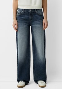 Breda denimjeans i mörk tvätt med ljus blekning. Har fem fickor, bälteshällor och knappgylf. I kombination med vita sneakers.