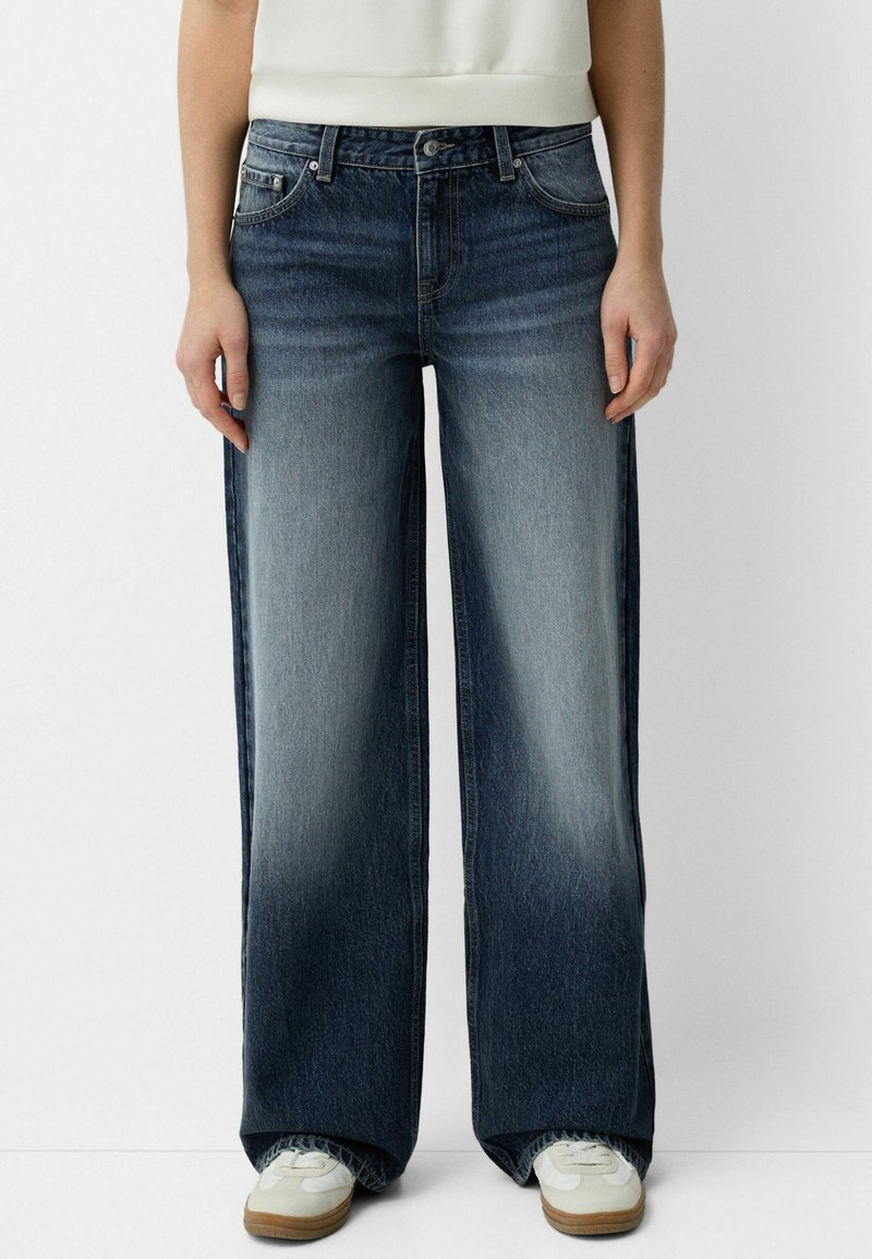 Breda denimjeans i mörk tvätt med ljus blekning. Har fem fickor, bälteshällor och knappgylf. I kombination med vita sneakers.