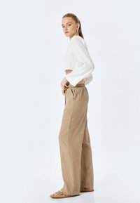 Witte crop top met lange mouwen, gecombineerd met lichtbruine wijde broek. De broek heeft een gestructureerde stof en een elastische taille, met zijzakken.