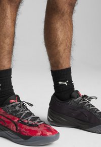Baskets de sport en camouflage noir et rouge avec une maille texturée et des superpositions synthétiques, accompagnées de chaussettes noires côtelées arborant un logo blanc.