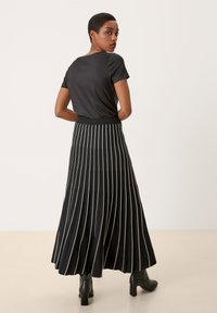 Zwarte top met korte mouwen en een ronde hals, gecombineerd met een lange, geplooide zwarte rok met witte verticale strepen. Zwarte high heels.