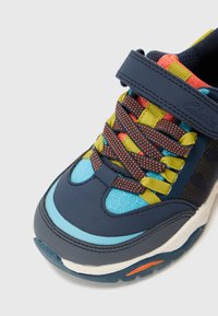 Marineblaue Sneakers mit hexagonalen blauen Akzenten, mehrfarbigen Netzschnürsenkeln, gepolsterter Zunge und Klettverschluss. Gepolsterte Sohle mit orangefarbenem Detail.