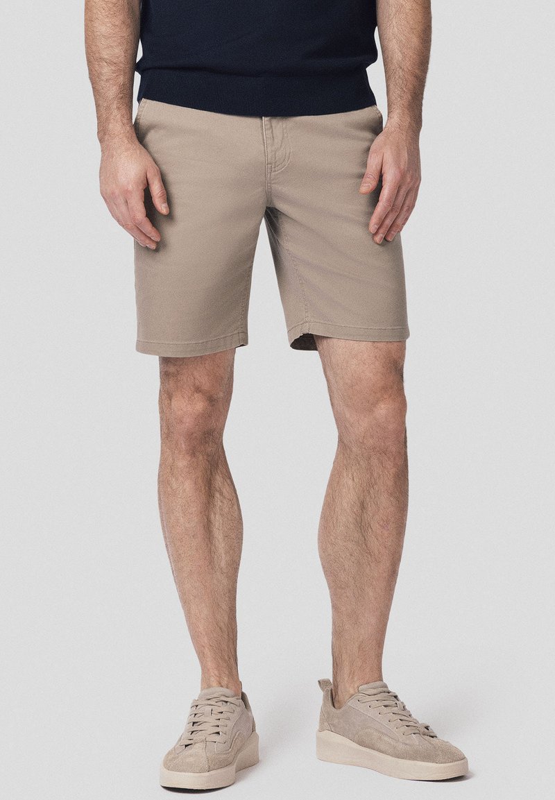 Beżowe bawełniane szorty o slim fit, długości do kolan, z bocznymi kieszeniami i subtelnymi detalami w szwie, w zestawieniu z jasnobeżowymi zamszowymi sneakersami.